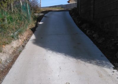 Egy betonút, amely egy házhoz vezet egy vidéki területen.
